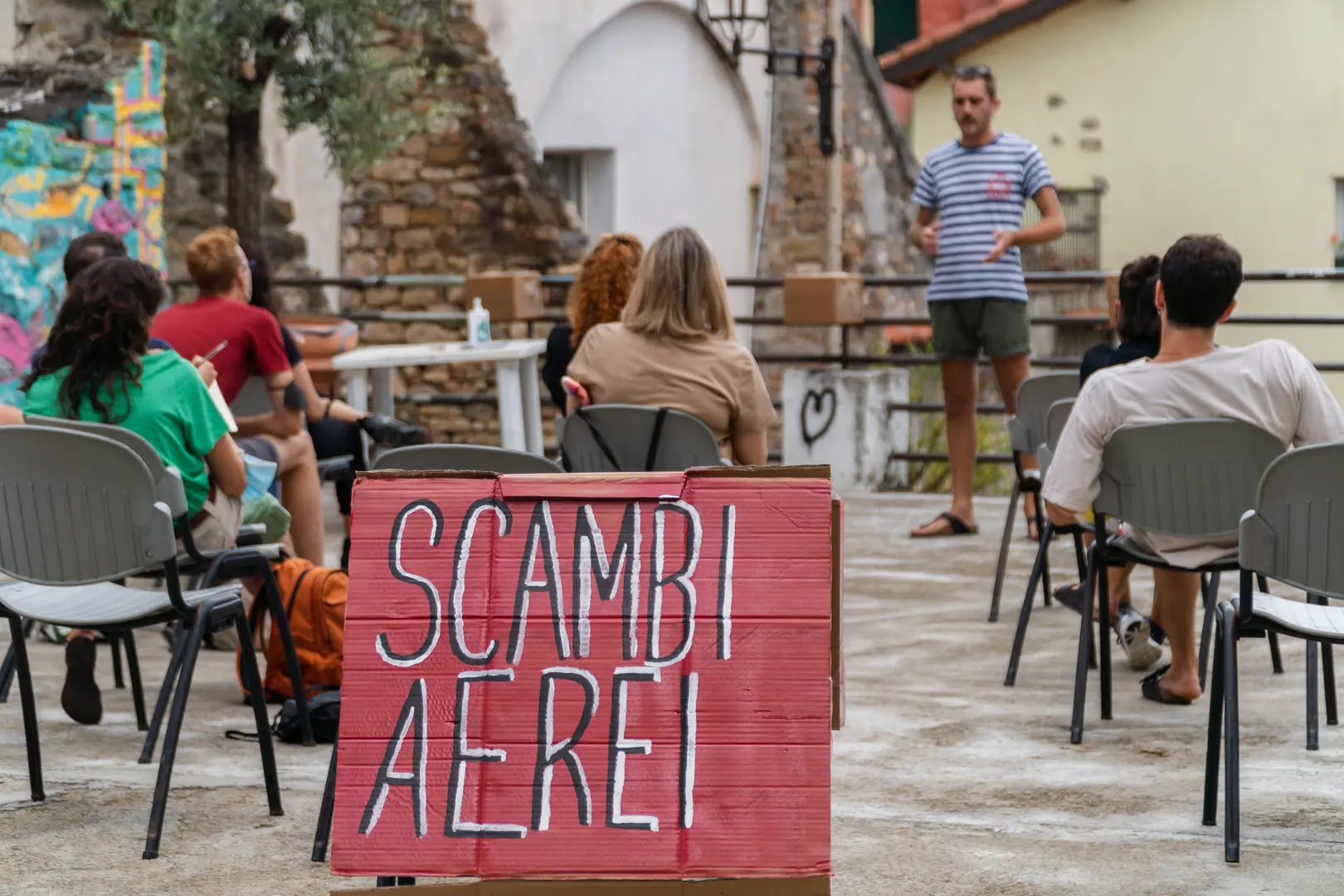 Gabriele Genduso che parla davanti al pubblico di Scambi e la scritta “Scambi Aerei” su un cartone in primo piano.